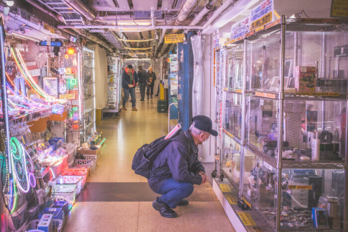 photo of an elderly man squatting to squint at old electronics at akihabara radio center