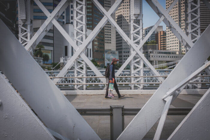 photo of man holding a skateboard while walking on a bridge