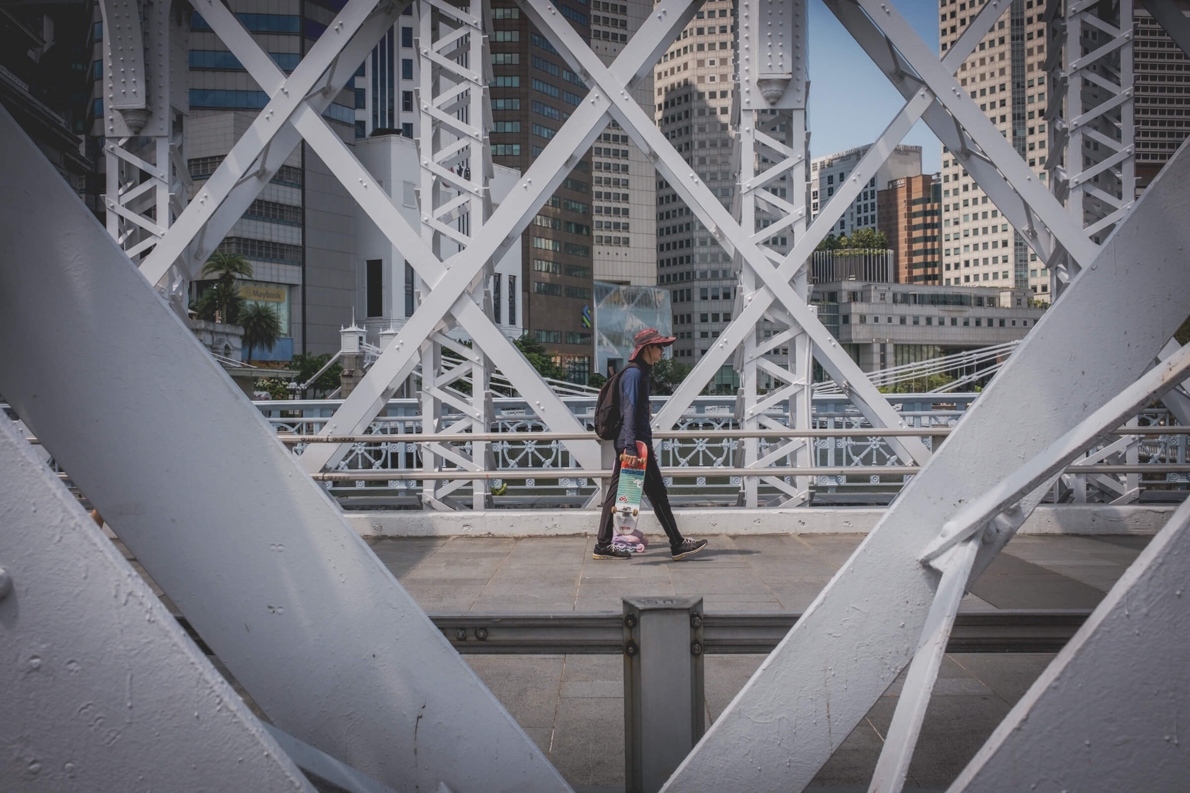 photo of man holding a skateboard while walking on a bridge