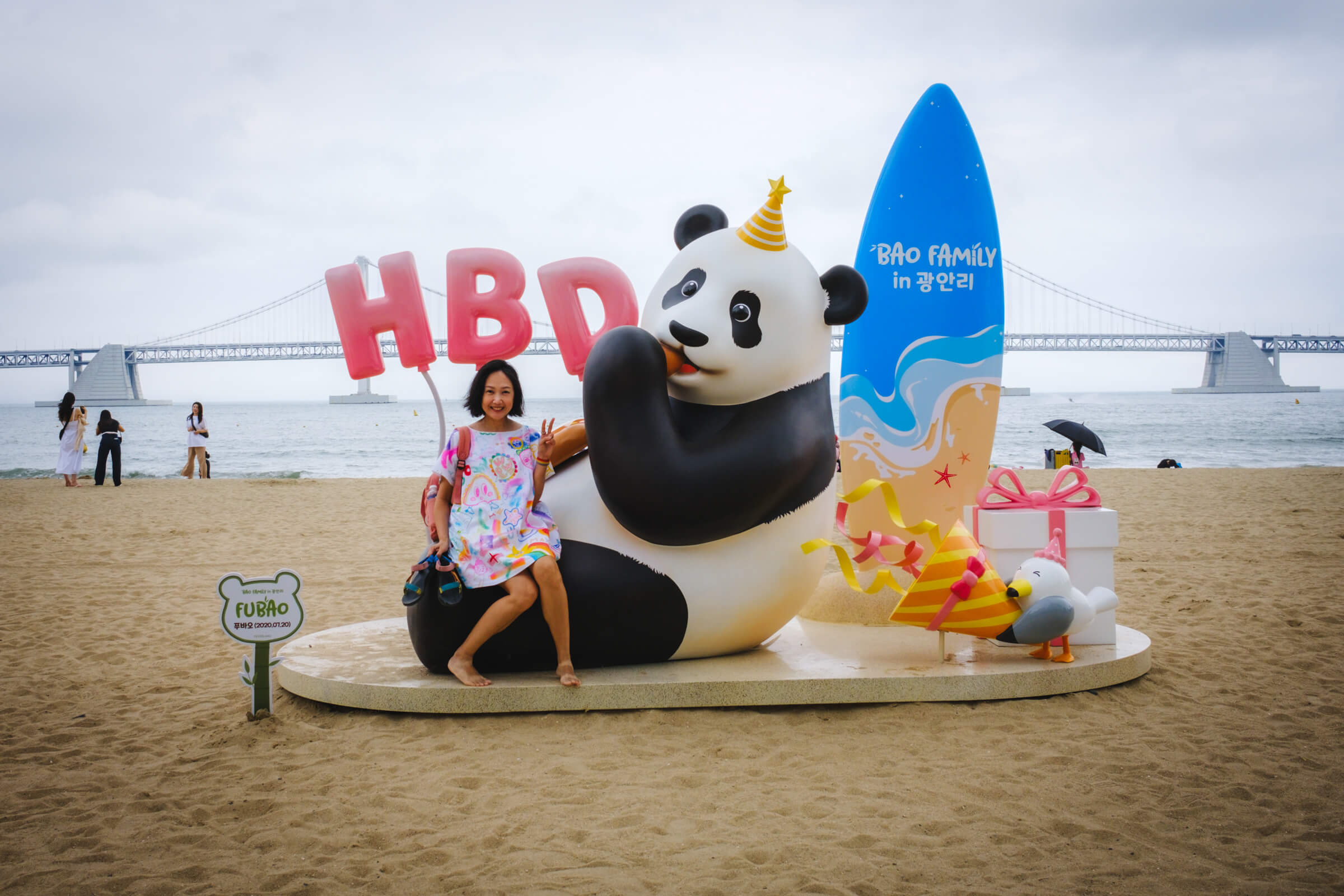photo of my partner posing with a "happy birthday" panda installation at the beach